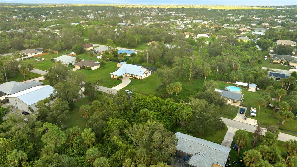 An aerial view shows a suburban neighborhood with houses, swimming pools, and dense green trees — 4355 MELIS STREET, PORT CHARLOTTE, FL