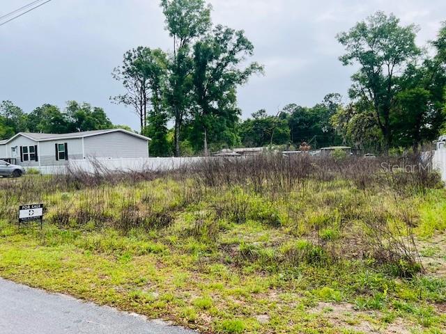 A vacant, overgrown lot sits in front of a white mobile home — Lot 4 NW 13th ST, OCALA, FL