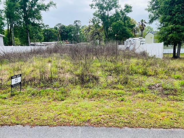 A vacant, overgrown lot with a for-sale sign sits in front of a white fence — Lot 4 NW 13th ST, OCALA, FL