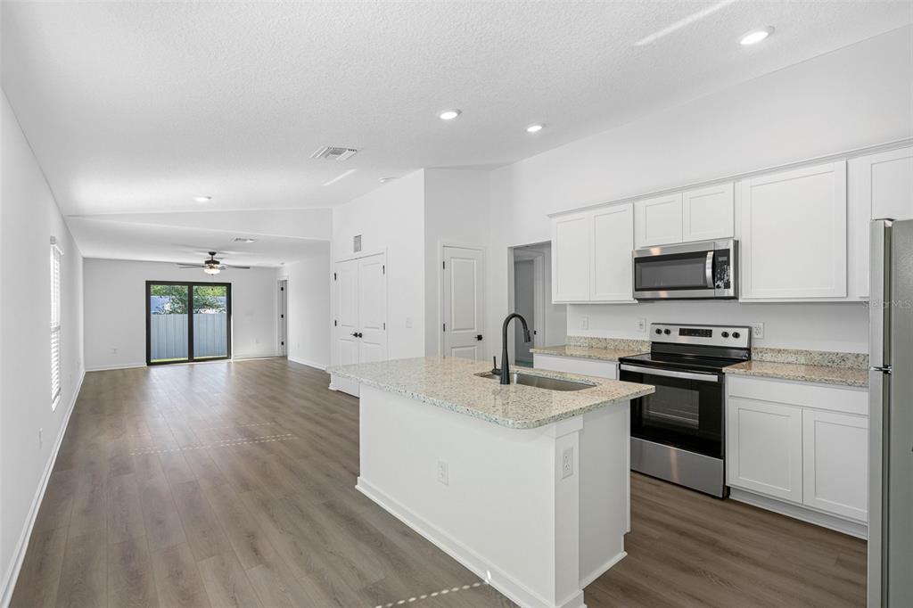 A kitchen with white cabinets and granite countertops overlooks an open-concept living area with flooring — 7154 CANOPY LANE, LAKELAND, FL