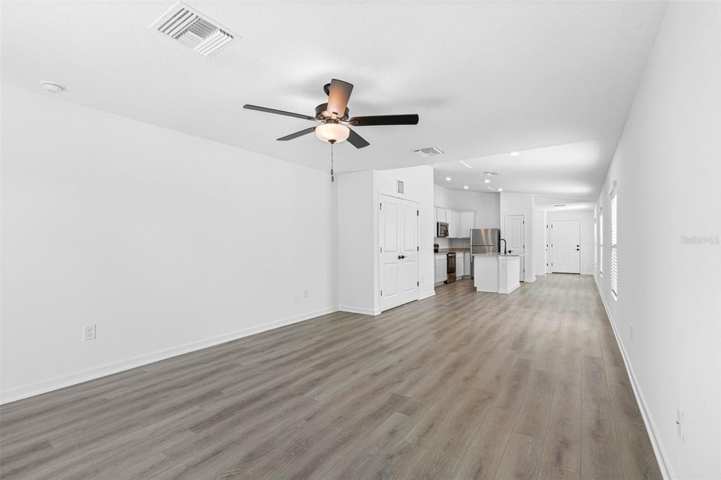 A bright, open-concept living area features light wood-look flooring, a ceiling fan, and a kitchen — 7154 CANOPY LANE, LAKELAND, FL