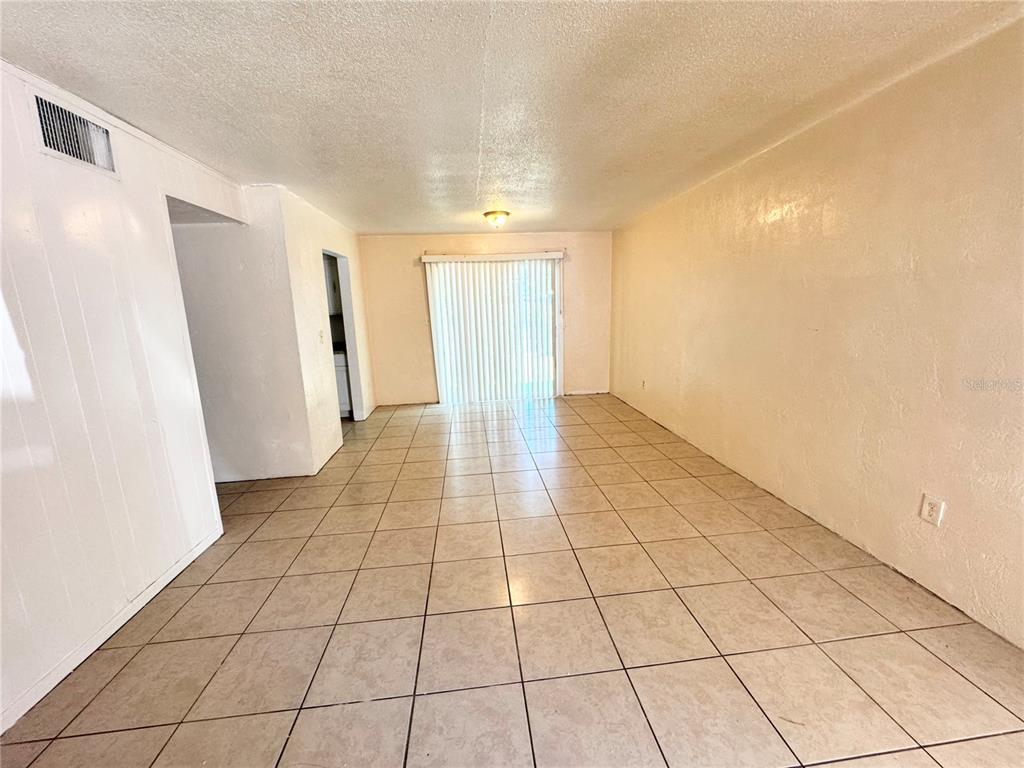An empty room with beige tile flooring, white walls, and a sliding glass door — 1229 KENNEDY ROAD UNIT 43, DAYTONA BEACH, FL