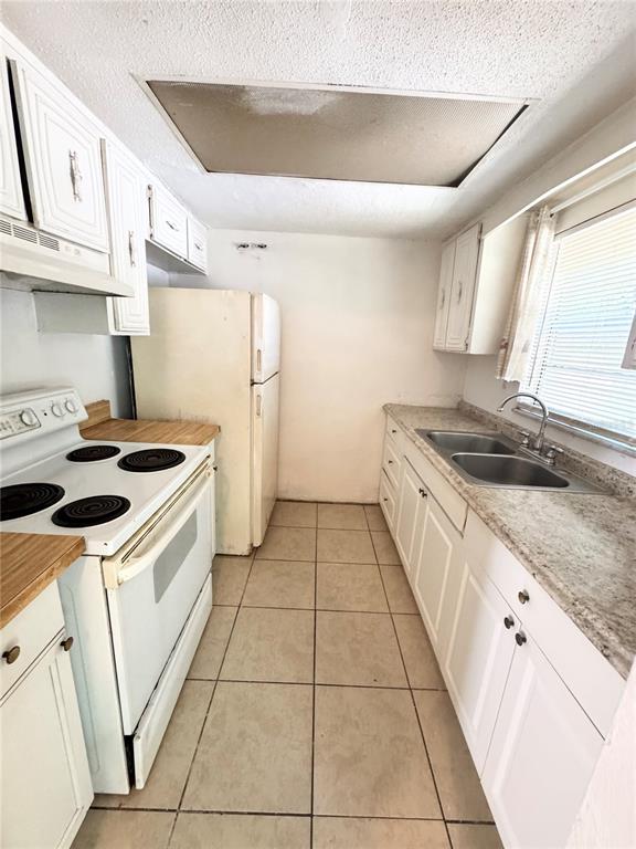 A kitchen features white cabinets, a white electric stove, a refrigerator, and tiled flooring — 1229 KENNEDY ROAD UNIT 43, DAYTONA BEACH, FL