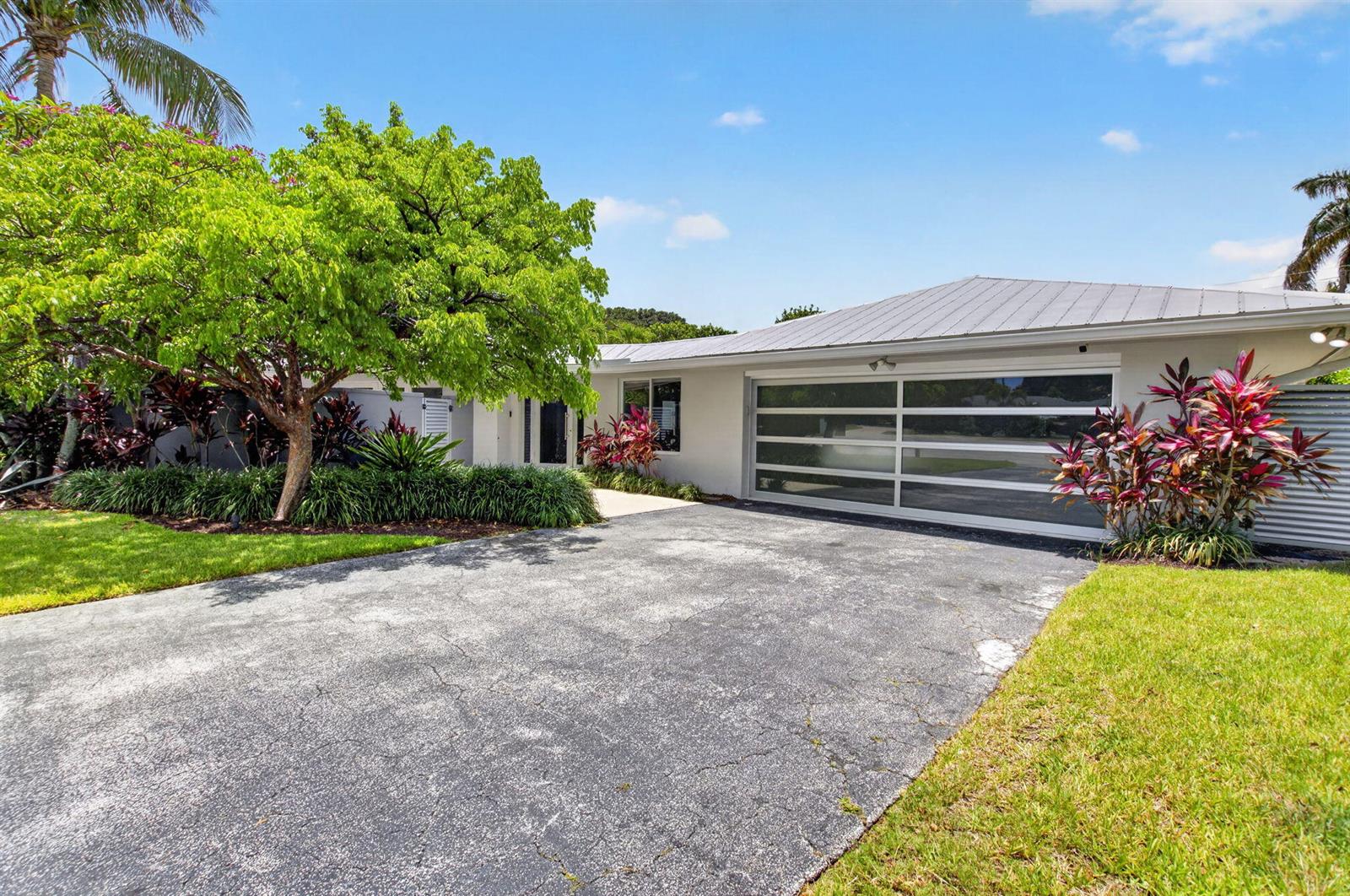 A paved driveway leads to a house with a modern glass-paneled garage door and landscaping — 2006 NW 3rd Avenue, Delray Beach FL 33444, DELRAY BEACH, FL
