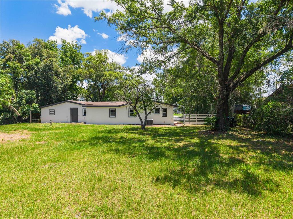 A single-story house with a white exterior sits on a grassy lot with large trees — 842 DENNIS AVENUE, ORLANDO, FL