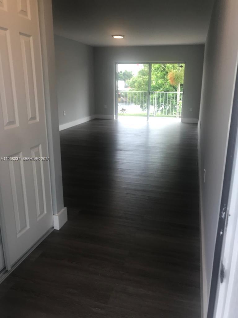 An empty room with dark wood-look flooring leads to a sliding glass door and balcony — 7570 SW 82nd St # F209, Miami FL 33143, MIAMI, FL