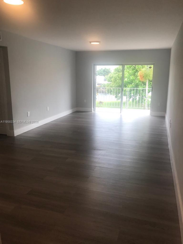 An empty room with gray walls, dark wood-look flooring, and a sliding glass balcony door — 7570 SW 82nd St # F209, Miami FL 33143, MIAMI, FL