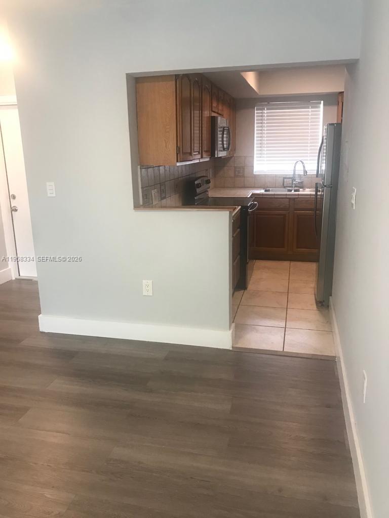 A kitchen with wood cabinets and tile flooring is viewed from an adjacent living area — 7570 SW 82nd St # F209, Miami FL 33143, MIAMI, FL