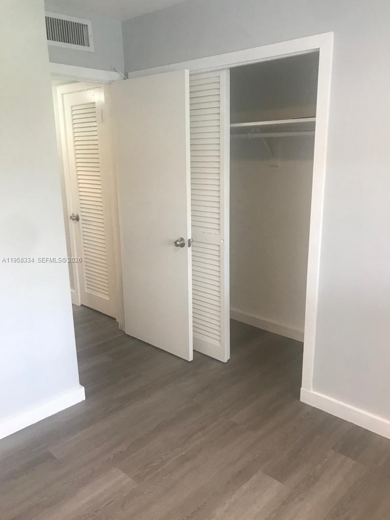 This room features light gray walls, wood-look flooring, and a closet with white louvered doors — 7570 SW 82nd St # F209, Miami FL 33143, MIAMI, FL