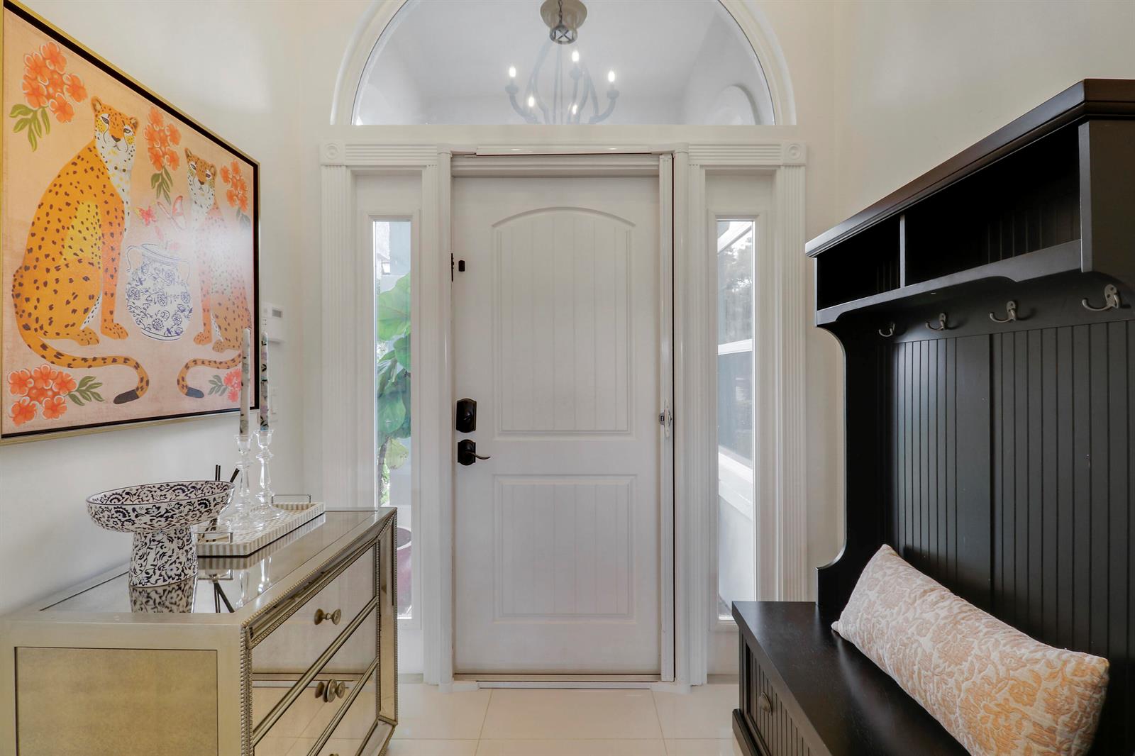 An entryway features a white front door, a mirrored chest, and a black hall tree — 1560 Wilderness Road, West Palm Beach FL 33409, WEST PALM BEACH, FL