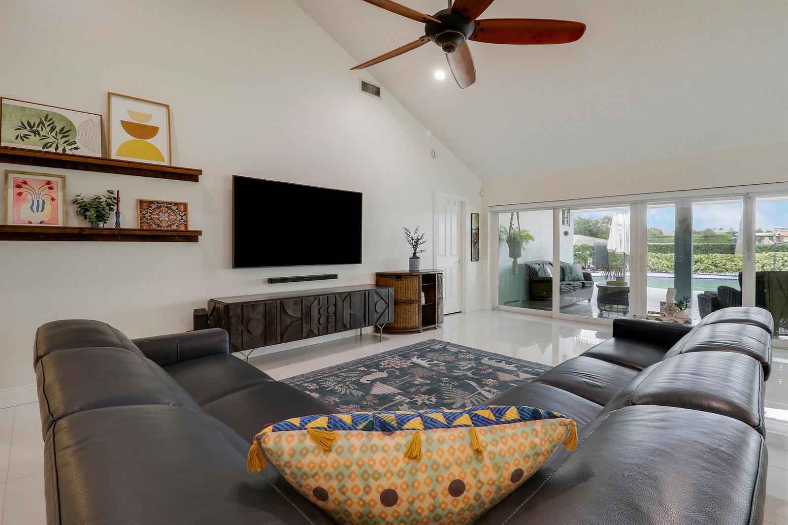 A living room features a vaulted ceiling, dark leather sectional, wall-mounted television, and sliding glass doors — 1560 Wilderness Road, West Palm Beach FL 33409, WEST PALM BEACH, FL