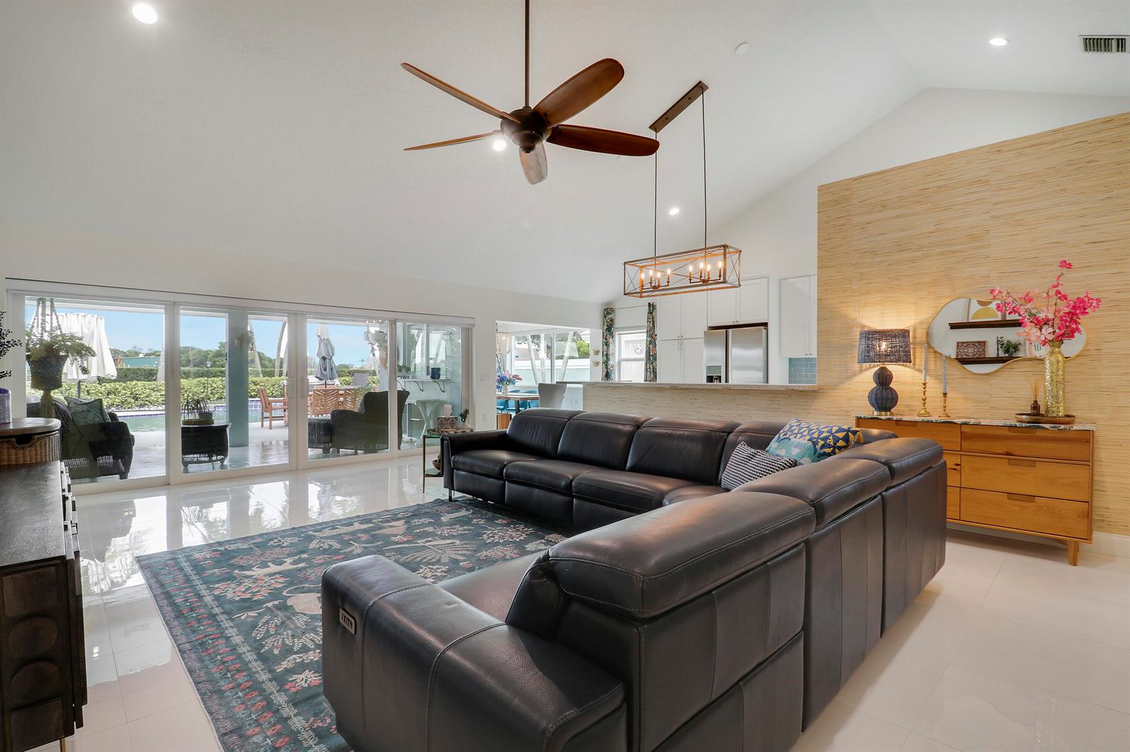 A spacious living room features a large leather sectional, vaulted ceilings, and sliding glass doors — 1560 Wilderness Road, West Palm Beach FL 33409, WEST PALM BEACH, FL