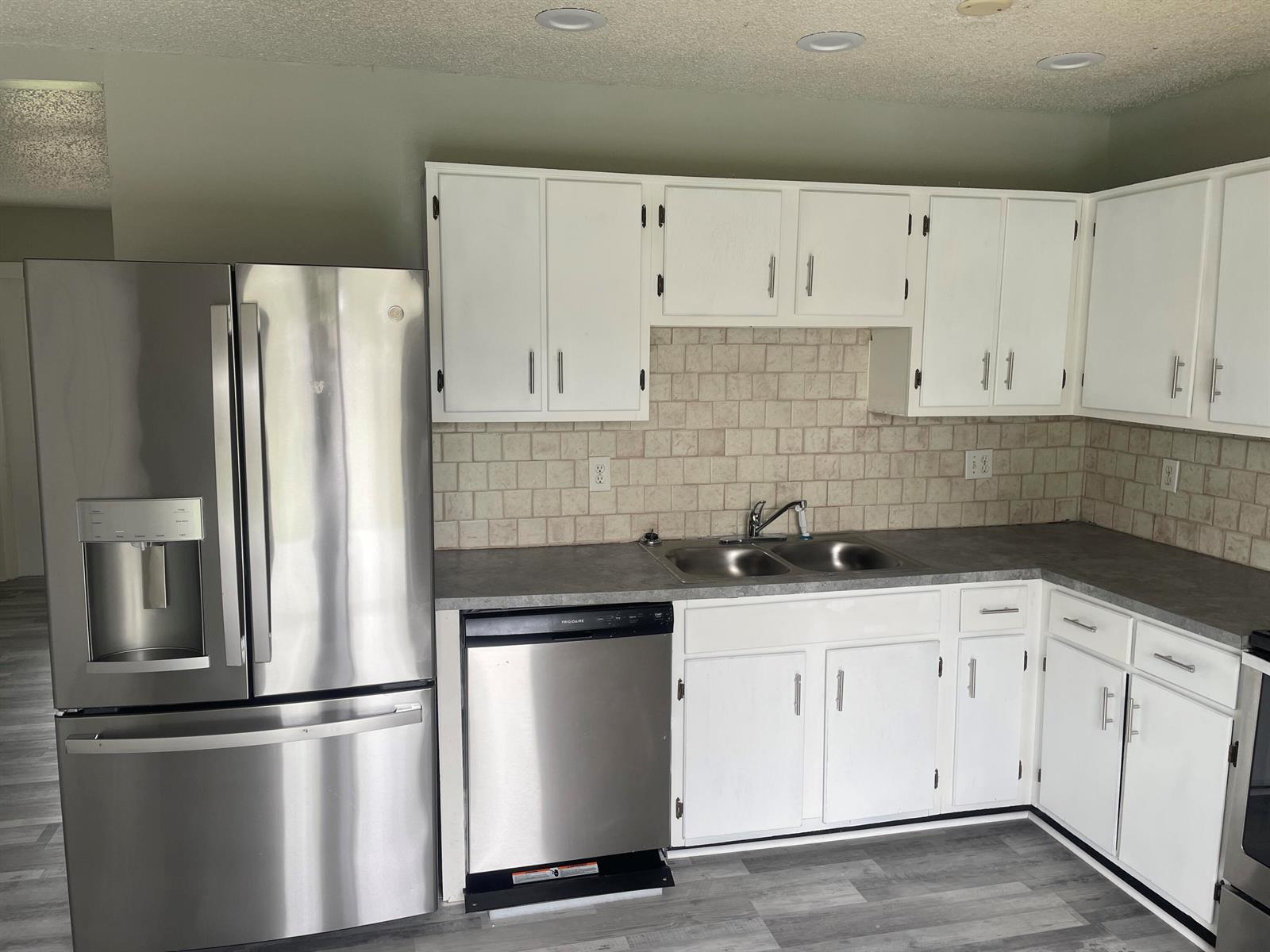 A kitchen features white cabinets, stainless steel appliances, a gray countertop, and a tiled backsplash — 3611 Jupiter Boulevard SE, Palm Bay FL 32909, PALM BAY, FL