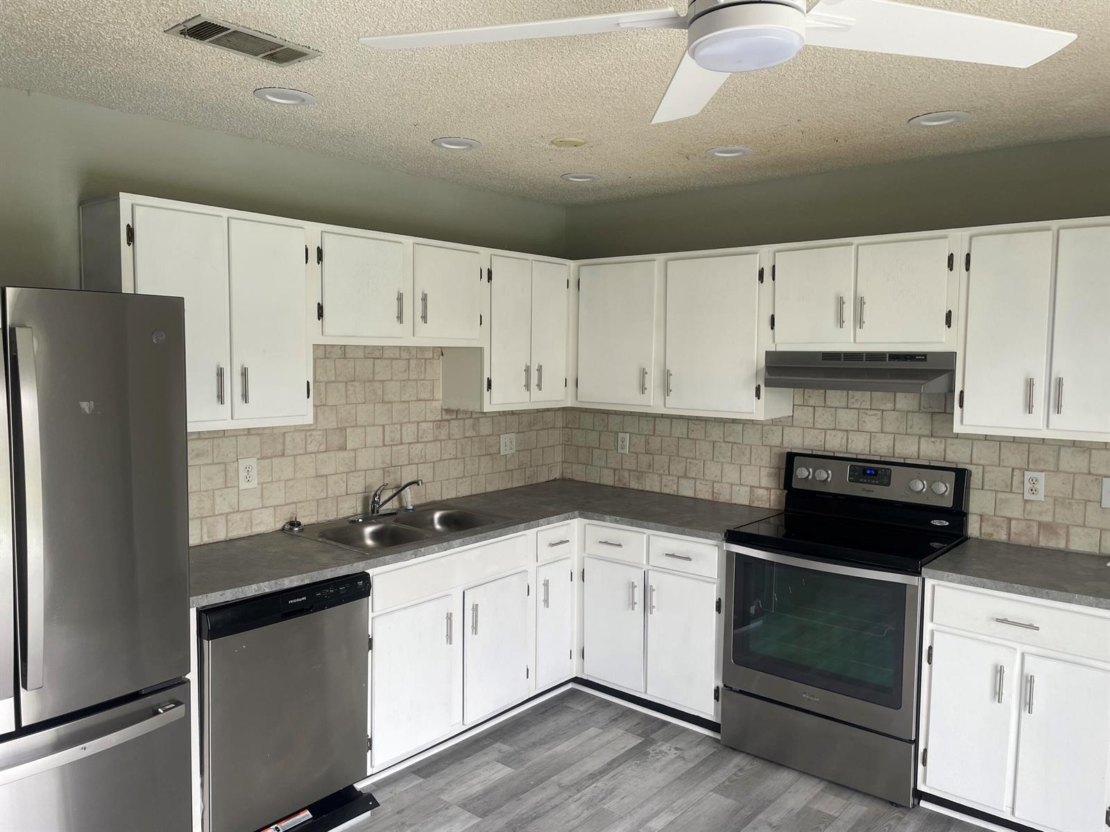 A kitchen features white cabinets, gray countertops, stainless steel appliances, and a tiled backsplash — 3611 Jupiter Boulevard SE, Palm Bay FL 32909, PALM BAY, FL