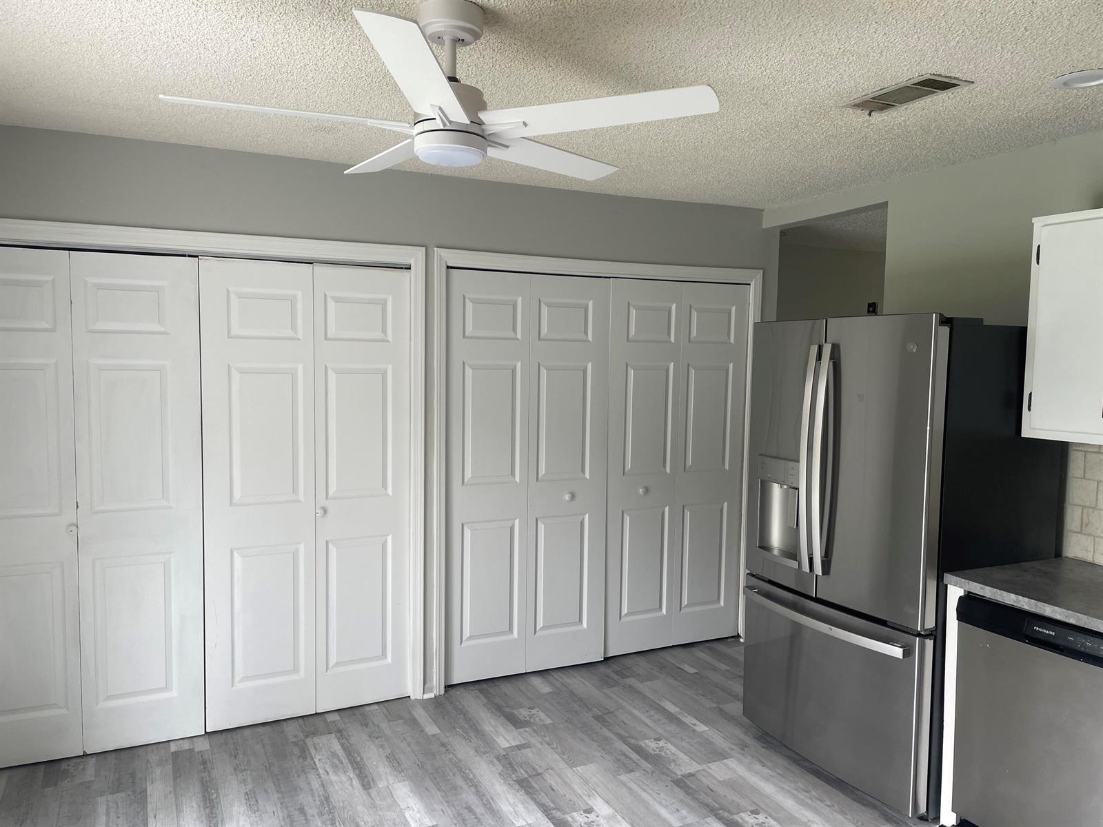 A room with grey wood-look flooring, two sets of white bifold doors, and a ceiling fan — 3611 Jupiter Boulevard SE, Palm Bay FL 32909, PALM BAY, FL