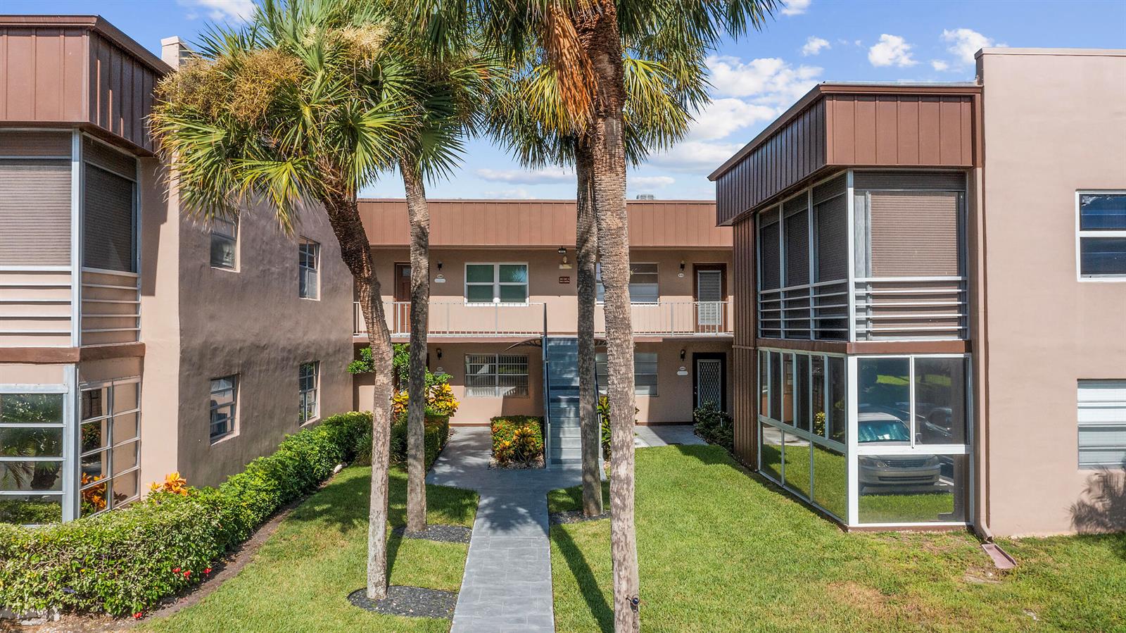 An exterior view of a two-story apartment complex with palm trees and a walkway — 344 Piedmont, Delray Beach FL 33484, DELRAY BEACH, FL