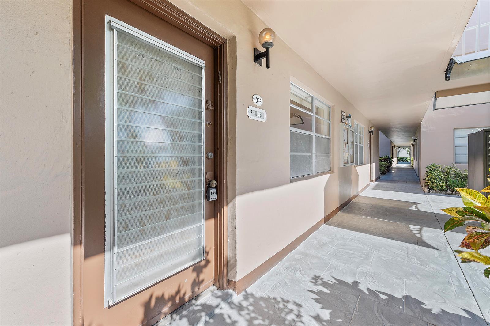 A brown front door with a security screen leads to an outdoor apartment building walkway — 344 Piedmont, Delray Beach FL 33484, DELRAY BEACH, FL
