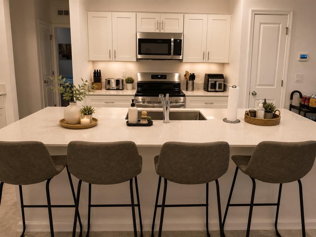A kitchen features a large island with bar seating, white cabinetry, and stainless steel appliances — 5782 LE MARIN WAY, KISSIMMEE, FL