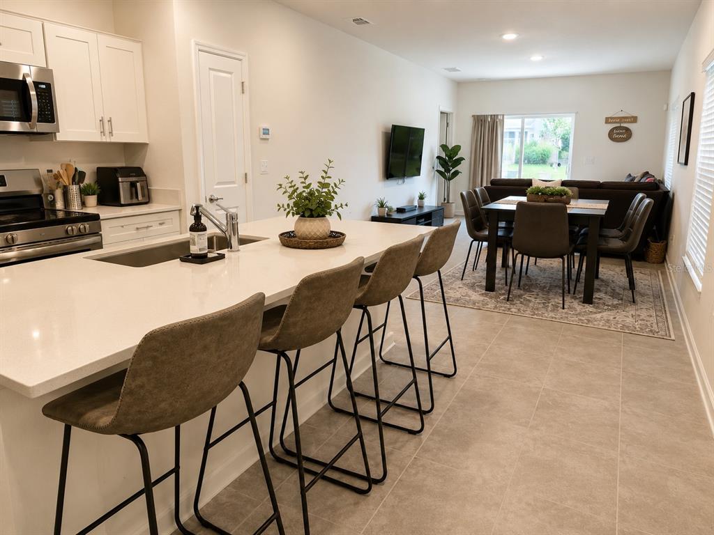 A kitchen with a large island and bar stools overlooks an open-concept dining and living area — 5782 LE MARIN WAY, KISSIMMEE, FL