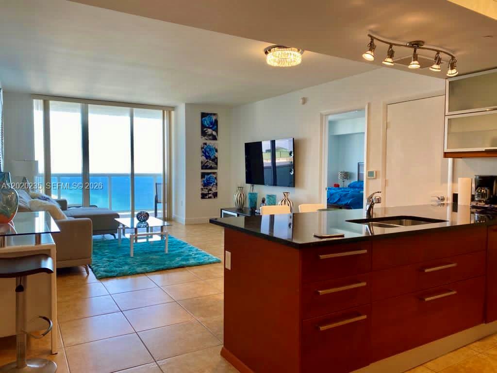A kitchen with dark wood cabinets and a granite island overlooks a living area — 1830 S Ocean Dr # 4810, Hallandale Beach FL 33009, HALLANDALE BEACH, FL