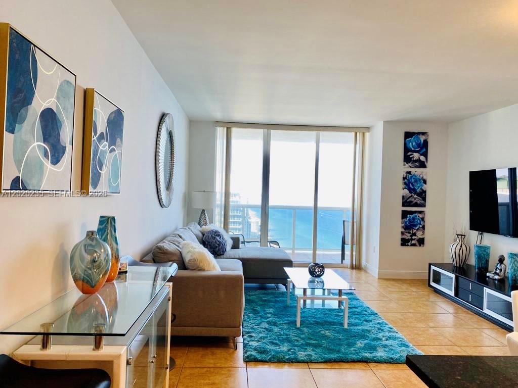 A living room features a grey sectional sofa, a blue rug, and a balcony view — 1830 S Ocean Dr # 4810, Hallandale Beach FL 33009, HALLANDALE BEACH, FL