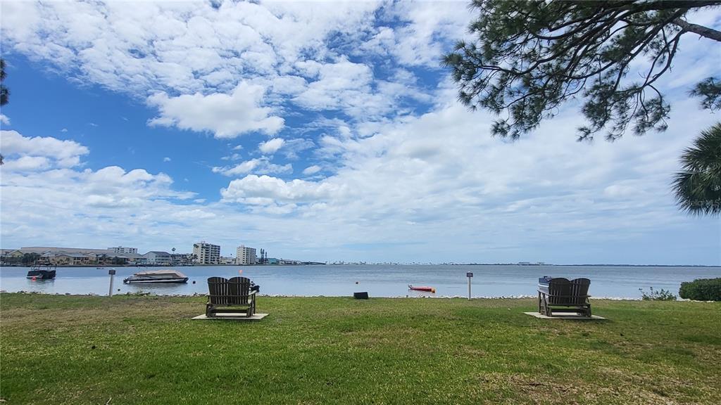 Two wooden chairs sit on a grassy lawn overlooking a calm bay with distant buildings — 2700 BAYSHORE BOULEVARD UNIT 592, DUNEDIN, FL