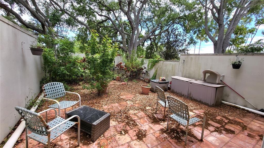 A patio with a tiled floor, outdoor furniture, and potted plants enclosed by high walls — 2700 BAYSHORE BOULEVARD UNIT 592, DUNEDIN, FL
