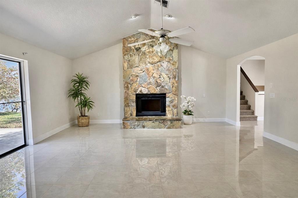 A living room features a stone fireplace, vaulted ceiling, tile flooring, and a sliding glass door — 513 BAR DRIVE, POINCIANA, FL