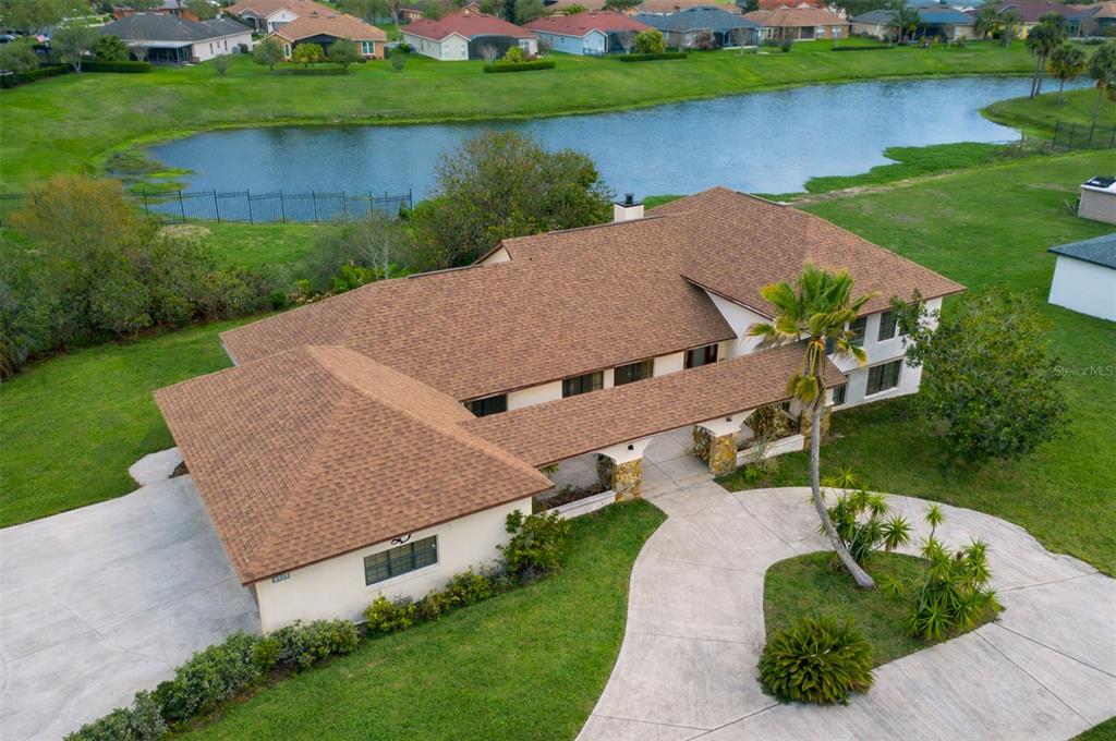 An aerial view shows a single-story house with a brown shingled roof near a pond — 513 BAR DRIVE, POINCIANA, FL