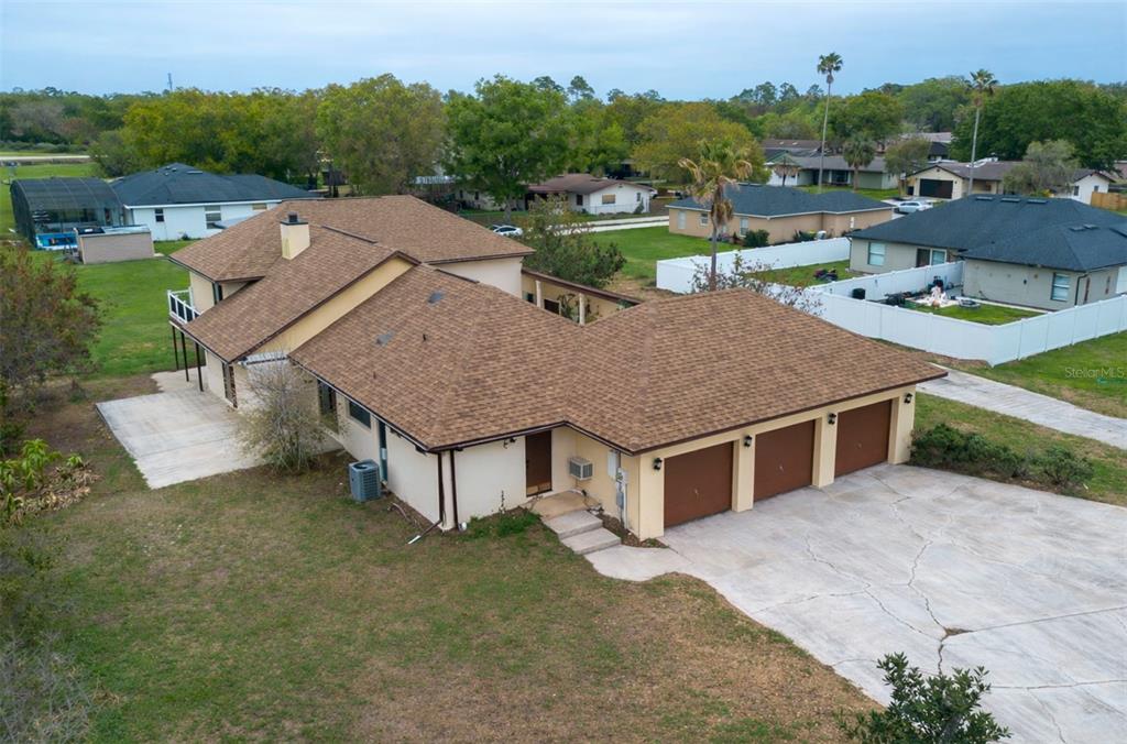 An aerial view shows a tan house with a brown shingled roof and three-car garage — 513 BAR DRIVE, POINCIANA, FL
