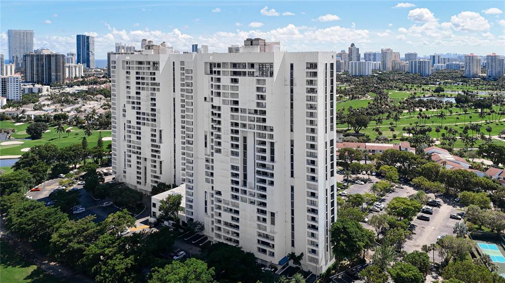 An aerial view of a tall white residential building surrounded by a golf course — 20225 NE 34TH COURT UNIT 817, MIAMI, FL