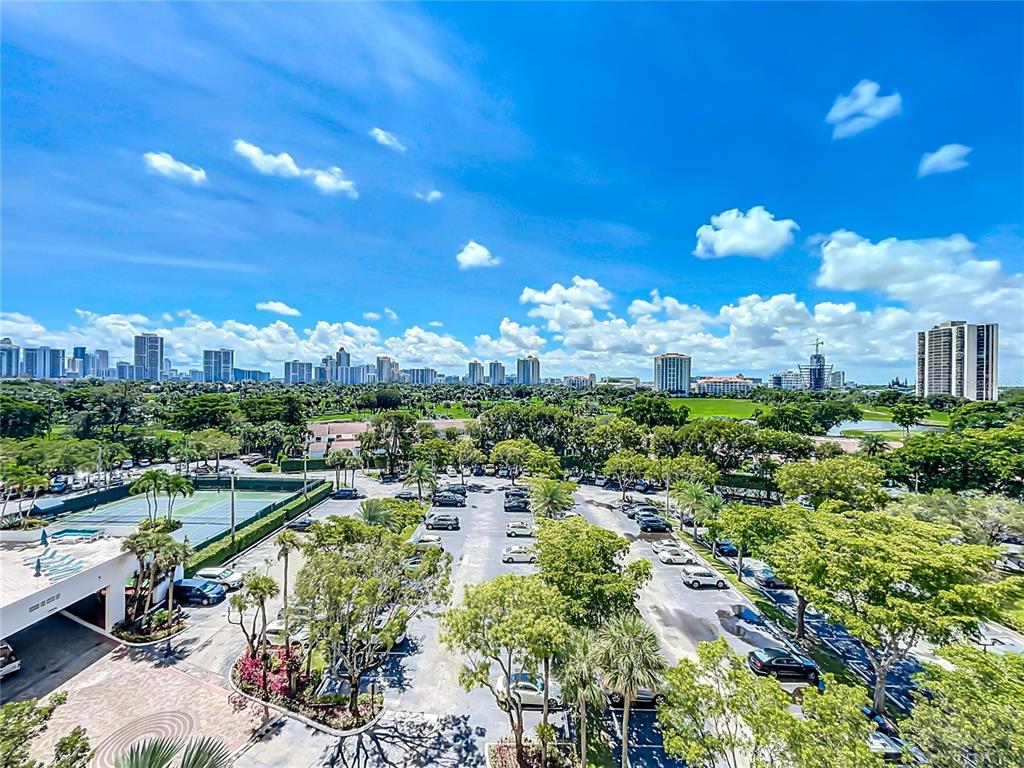 An elevated view shows a parking lot, tennis courts, and lush trees before a city skyline — 20225 NE 34TH COURT UNIT 817, MIAMI, FL