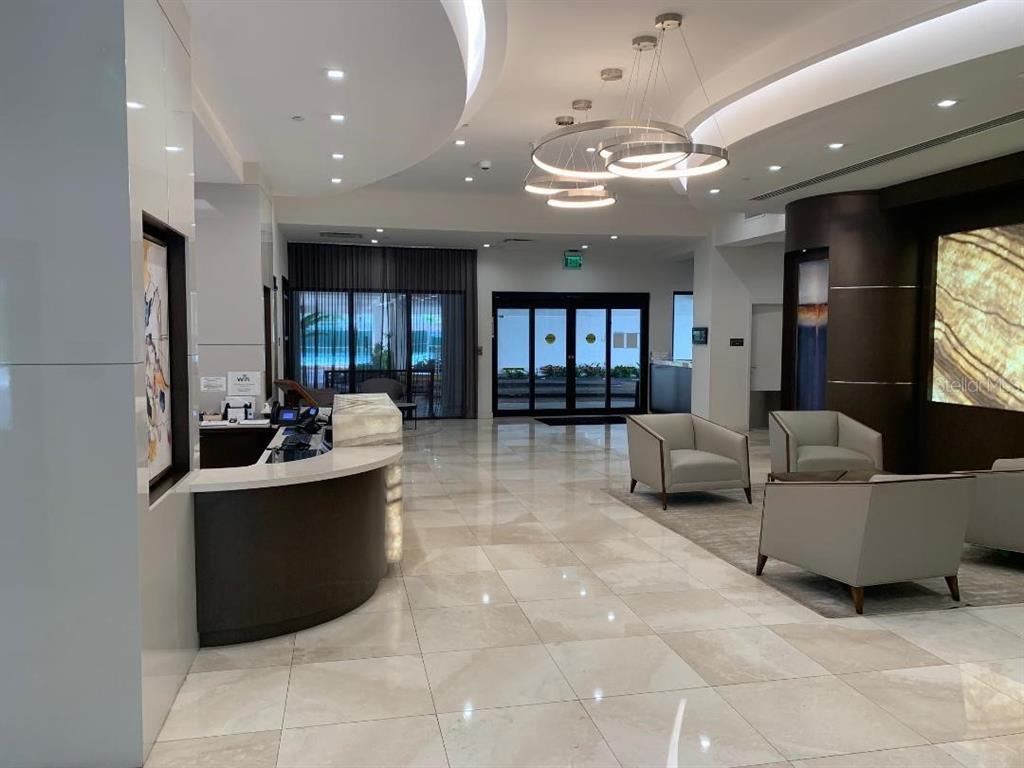 A modern building lobby features a curved reception desk, tile flooring, and contemporary seating areas — 20225 NE 34TH COURT UNIT 817, MIAMI, FL