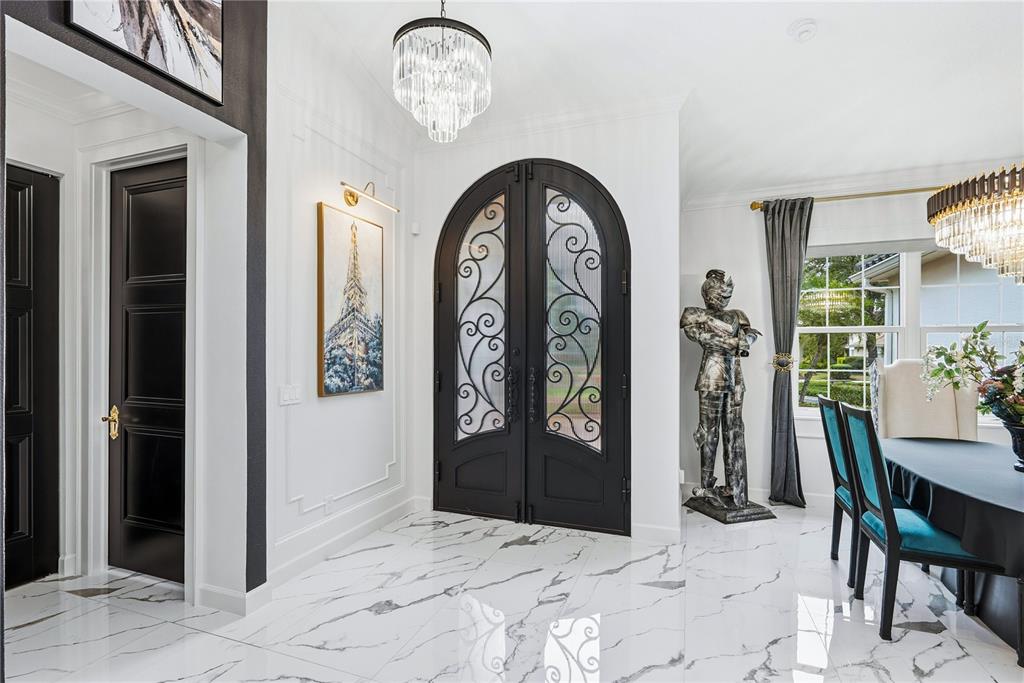 An entryway features marble floors, a double arched door, a chandelier, and a suit of armor — 7719 LATROBE COURT, LAKEWOOD RANCH, FL