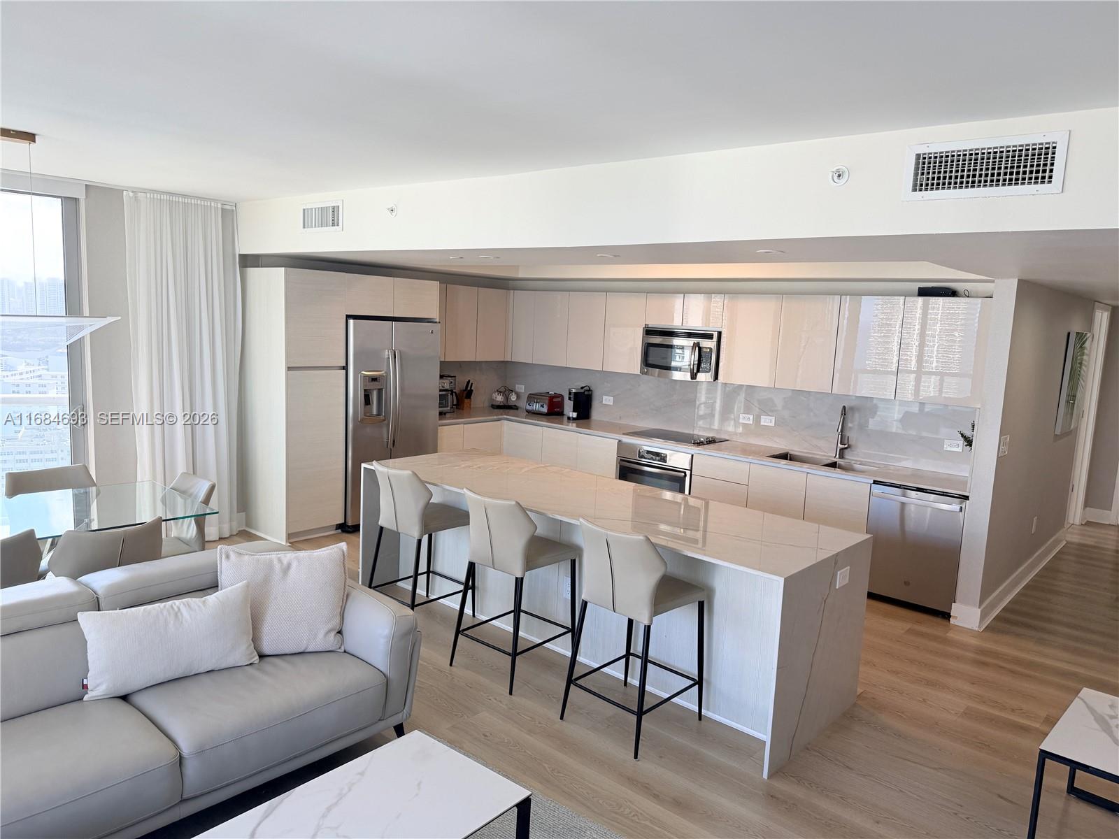 A modern open-concept kitchen features light wood cabinetry, a stone island, and stainless steel appliances — 2600 E Hallandale Beach blvd # T2701, Hallandale Beach FL 33009, HALLANDALE BEACH, FL