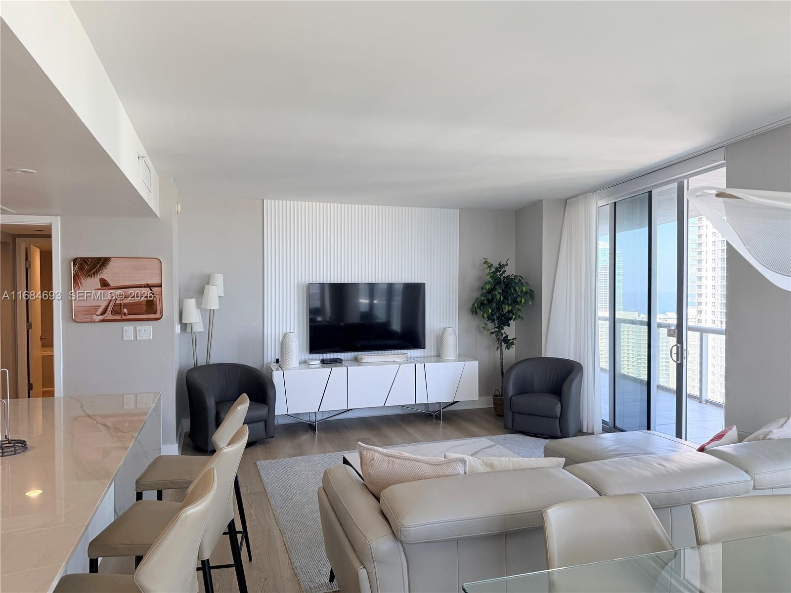 A modern living room features a white slatted accent wall, a television, and neutral furniture — 2600 E Hallandale Beach blvd # T2701, Hallandale Beach FL 33009, HALLANDALE BEACH, FL