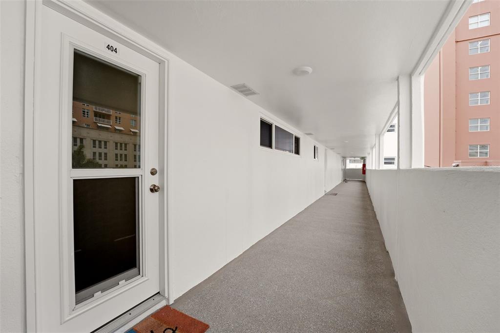 A white door labeled 404 opens onto a long, covered outdoor walkway with concrete flooring — 33 S GULFSTREAM AVENUE UNIT 404, SARASOTA, FL