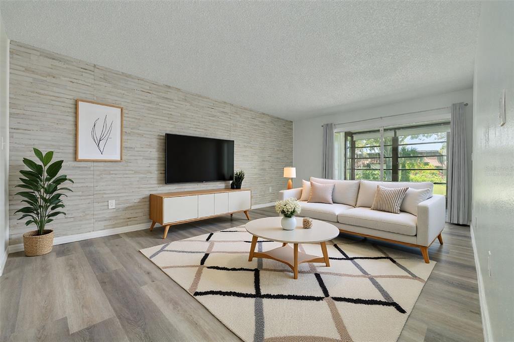 A living room features a textured accent wall, a television, a sofa, and a patterned rug — 7131 DELL ROAD UNIT 2, NEW PORT RICHEY, FL