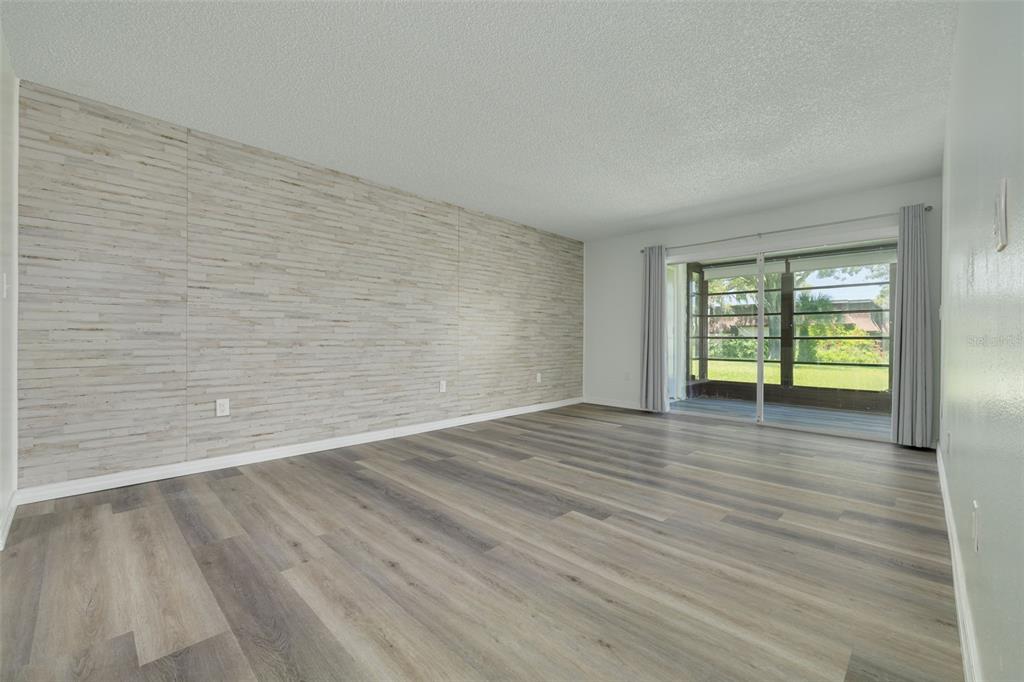 An empty living room features wood-look flooring, a textured accent wall, and sliding glass doors — 7131 DELL ROAD UNIT 2, NEW PORT RICHEY, FL
