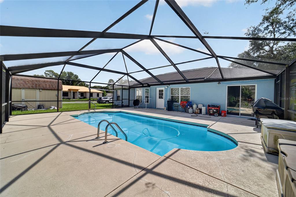 A swimming pool with a metal screen enclosure sits on a concrete patio behind a house — 304 MARION OAKS COURSE, OCALA, FL
