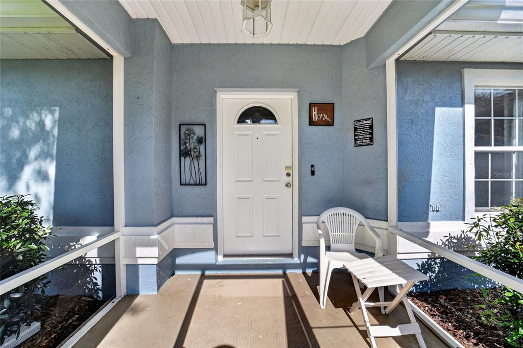 A covered front porch with blue stucco walls, a white door, and a white chair — 304 MARION OAKS COURSE, OCALA, FL