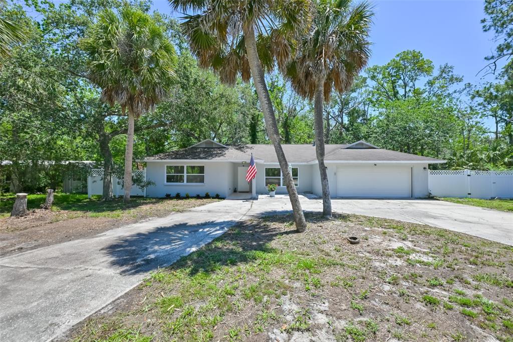 A single-story house with a white exterior, a two-car garage, and palm trees in front — 1578 INDIAN BAY ROAD, SPRING HILL, FL