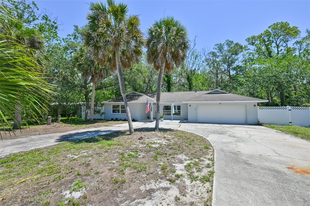 A single-story house with a white garage, palm trees, and a concrete driveway — 1578 INDIAN BAY ROAD, SPRING HILL, FL