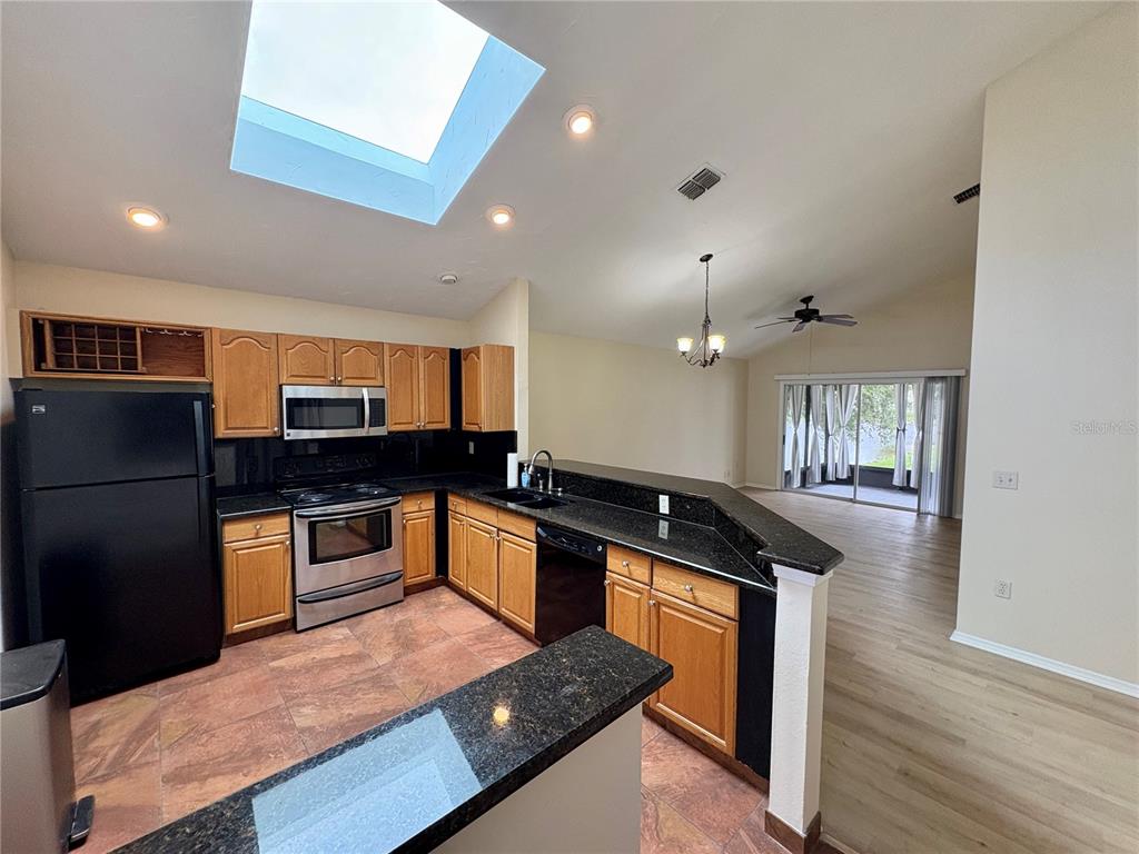 A kitchen with wood cabinets, black appliances, and granite countertops features a skylight above — 4007 39TH STREET W, BRADENTON, FL