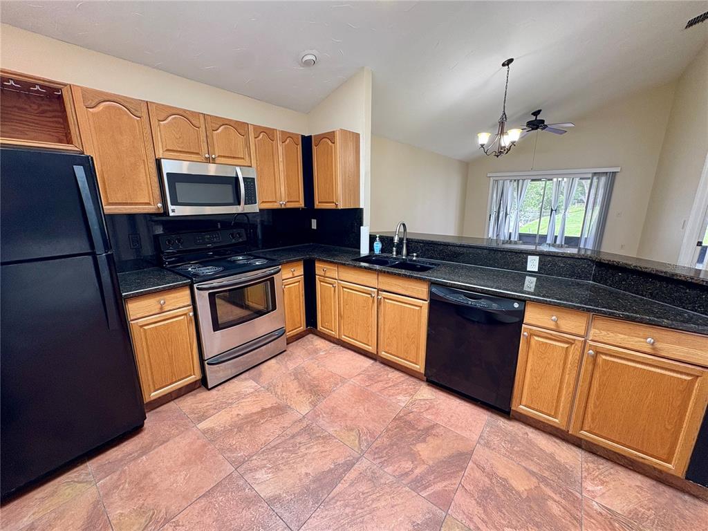 A kitchen features oak cabinets, black appliances, dark granite countertops, and reddish-brown tile flooring — 4007 39TH STREET W, BRADENTON, FL