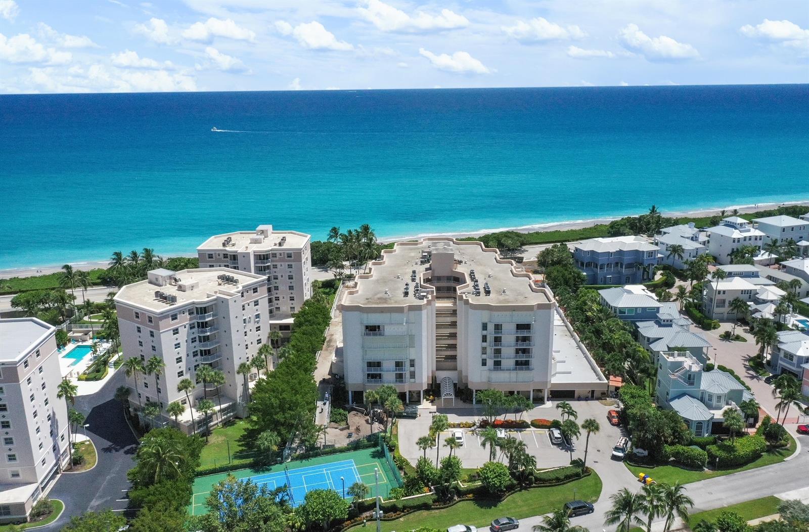 An aerial view shows multi-story apartment buildings near a beach with a tennis court below — 176 Helios Drive # 102, Jupiter FL 33477, JUPITER, FL