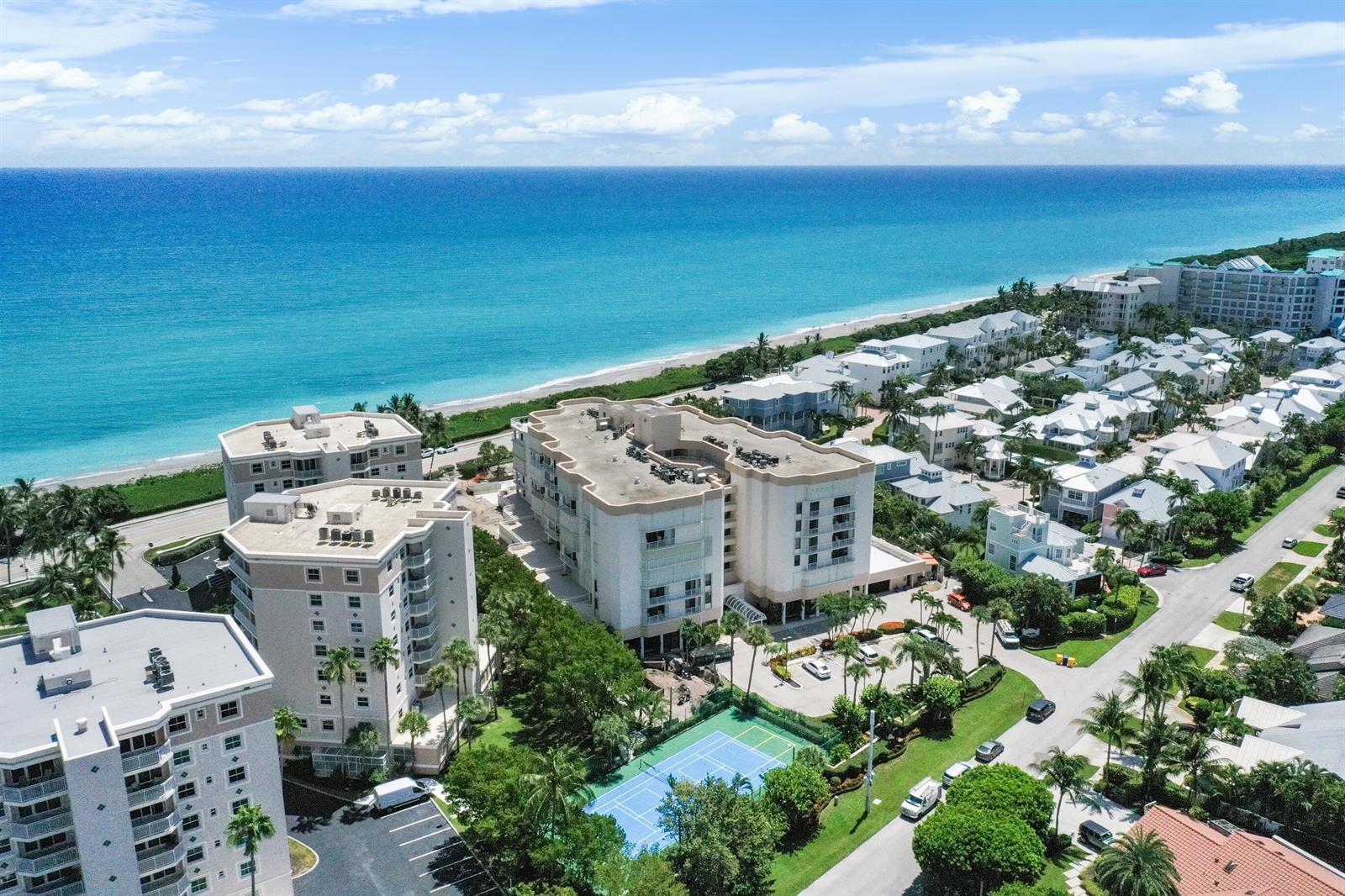 An aerial view shows several multi-story residential buildings near a beach and a tennis court — 176 Helios Drive # 102, Jupiter FL 33477, JUPITER, FL
