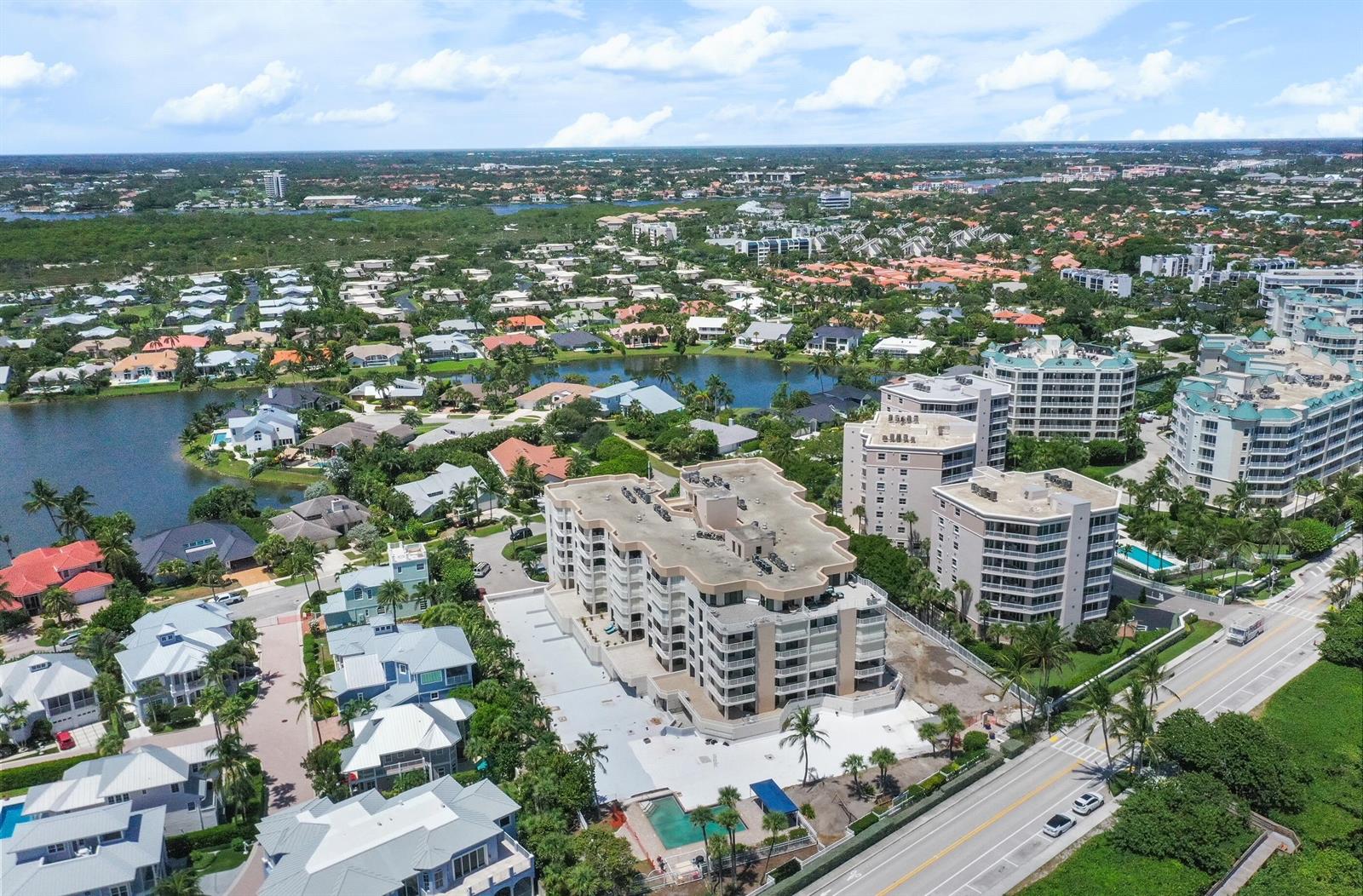 An aerial view shows a multi-story apartment complex surrounded by residential homes and a lake — 176 Helios Drive # 102, Jupiter FL 33477, JUPITER, FL