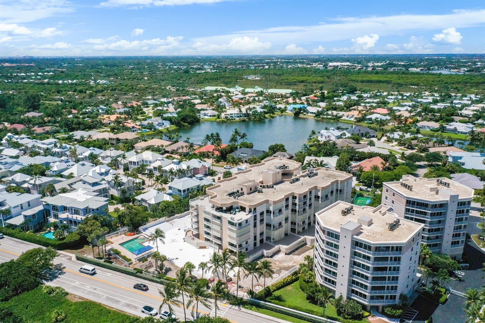 An aerial view shows multi-story residential buildings near a lake and a coastal road — 176 Helios Drive # 102, Jupiter FL 33477, JUPITER, FL