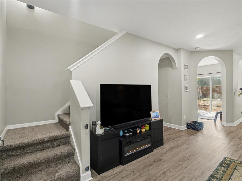 A living room features a carpeted staircase, a television on a media console, and arched doorways — 8430 QUARTER HORSE DRIVE, RIVERVIEW, FL